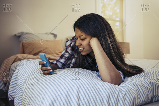 Young woman looking at her phone while lying on her bed