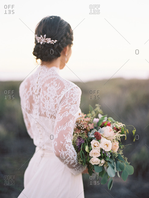 Bride holding bouquet, standing and looking out over the ocean