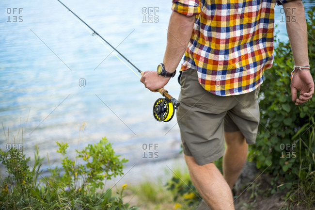 Man walking to water\'s edge with fishing pole