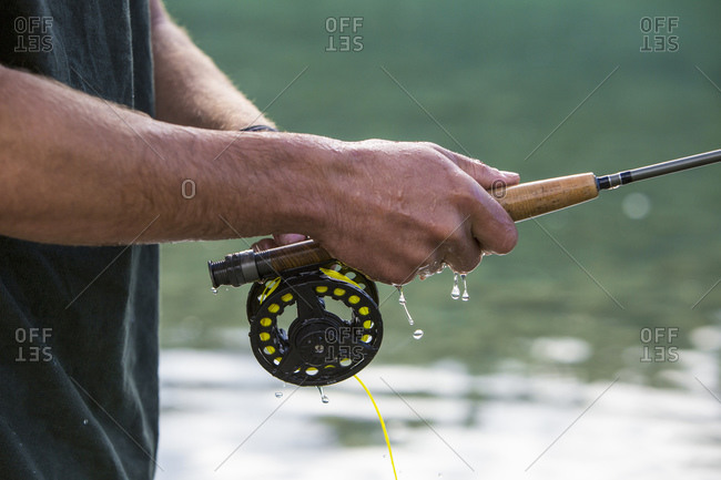 Water dripping from man's hand holding a fly fishing pole - Stock