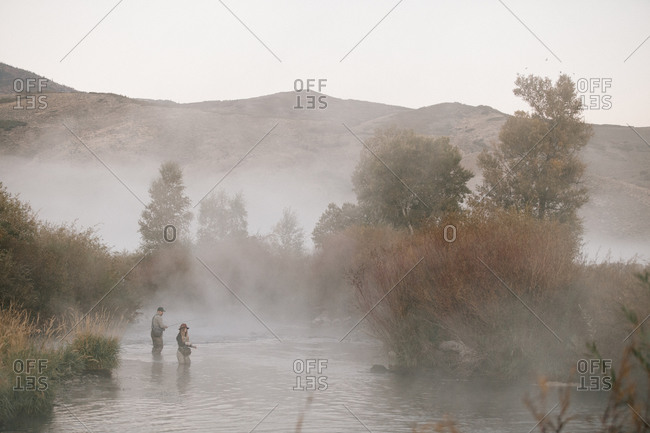 Man and woman fly fishing in a mist covered river