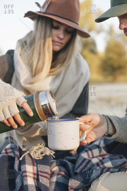 Woman pouring a hot drink from a vacuum flask into a cup on a winter picnic