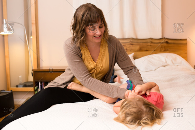 Mom tickling little girl on bed