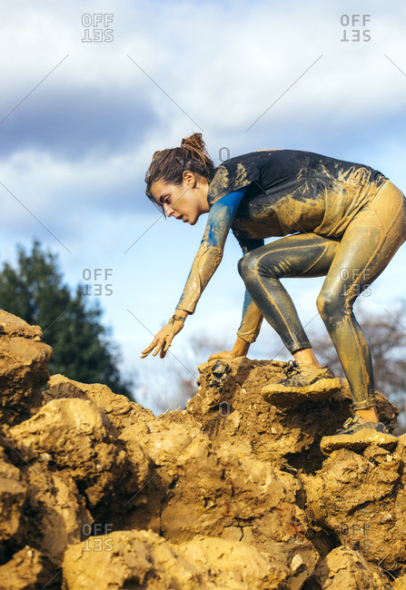 Woman in extreme obstacle race climbing down muddy rocks