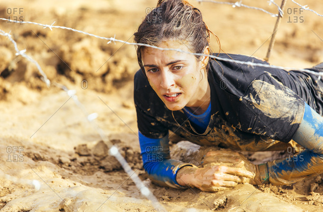 Woman in extreme obstacle race crawling under barbed wire