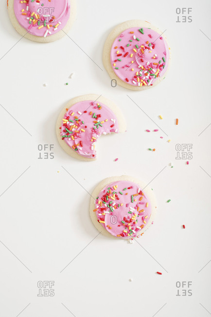 Sugar cookies with pink frosting and sprinkles with bite missing from one