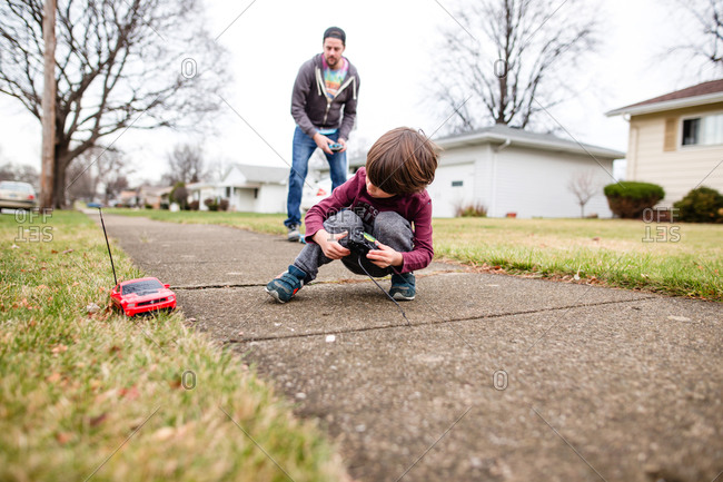 Boy and his father drive a remote controlled car on sidewalk