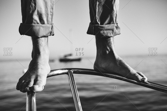 Feet of a man standing on the bow of a sailboat
