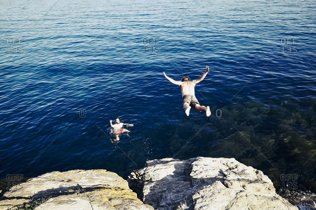 Young man jumping into the ocean to join his friend