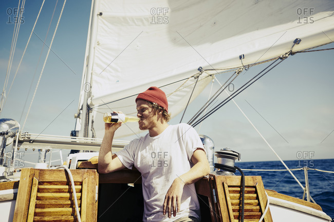 Young man standing at the cabin of a sailboat drinking a beer