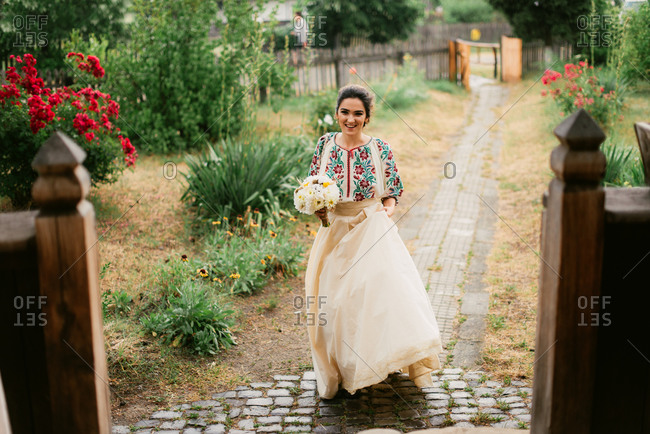 Bride in traditional Romanian embroidered blouse walking on garden path