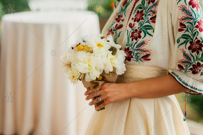 Close-up of bride in traditional Romanian blouse holding wedding bouquet