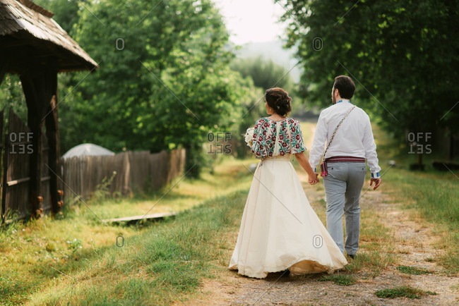Back view of bride and groom in traditional Romanian folk dress walking in farm