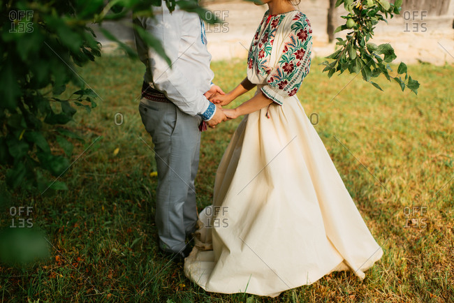 Romanian bride and groom hold hands under an apple tree