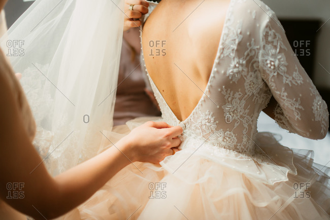 Woman zipping up bride\'s gown on her wedding day