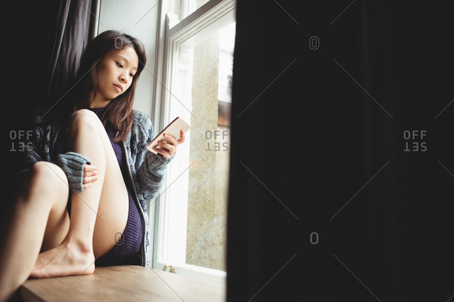 Brunette sitting on the edge of the window using smartphone at home