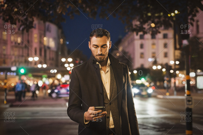 Man using smart phone on city street at night
