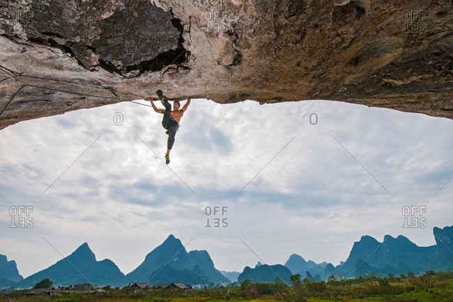 Scenic low angle view of rock climber hanging from an arch, White Mountain, Yangshuo, Guangxi Zhuang, China
