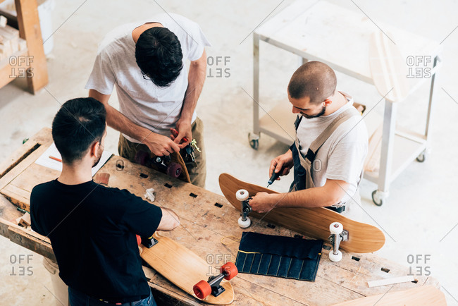 High angle view of young men standing around workbench attaching wheels to skateboards