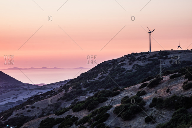 Wind turbines on mountain top against dramatic orange sky, Castelsardo, Sardinia, Italy
