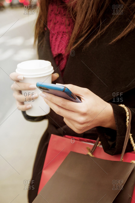 Close up of woman using cell phone while drinking coffee on the go