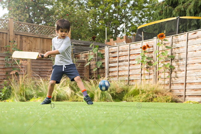 Boy playing cricket in garden with ball in mid air