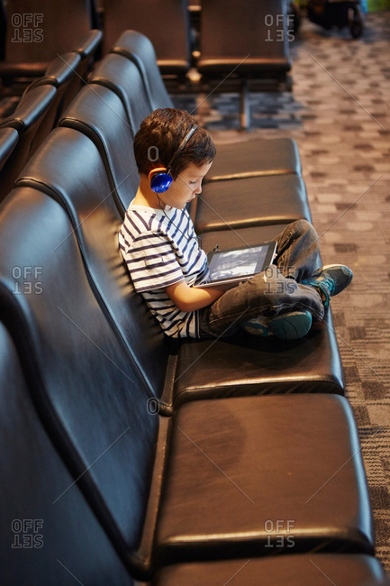 Young boy sitting in airport waiting area using digital tablet