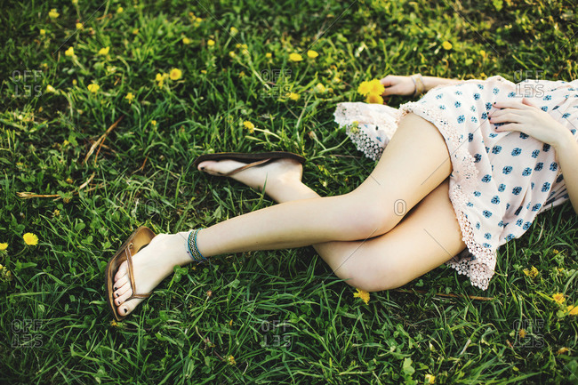 Waist down high angle view of young woman lying on grass wearing dress, flip flops and ankle bracelet