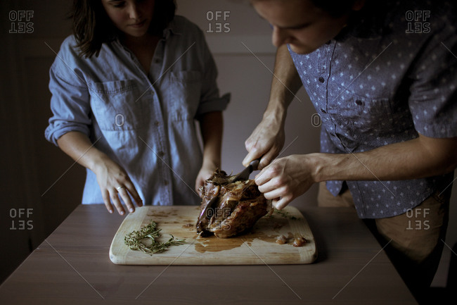 Couple cutting a portion of lamb on a cutting board