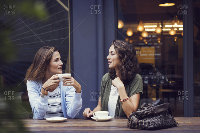 Two women talk over coffee outside a cafe