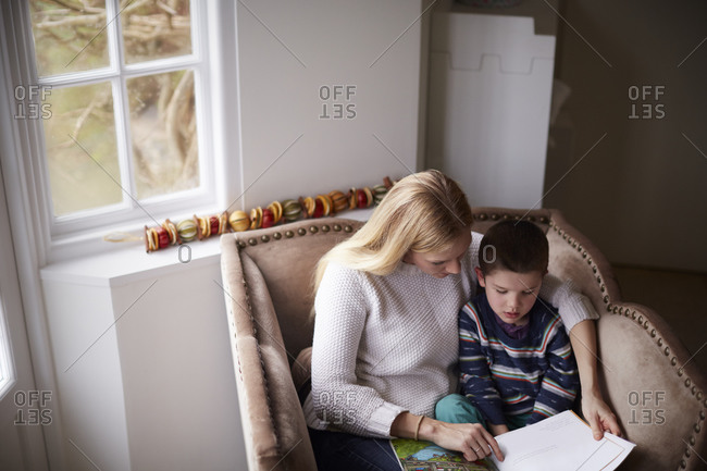 Mother sitting in chair at home reading story to her son