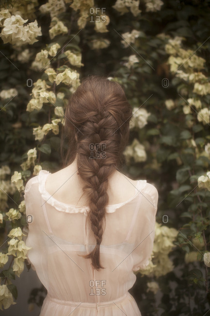 Woman with braided hair in a sheer dress looking at flowers in a garden