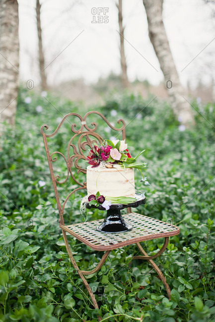 Cake decorated with burgundy flowers on chair in forest