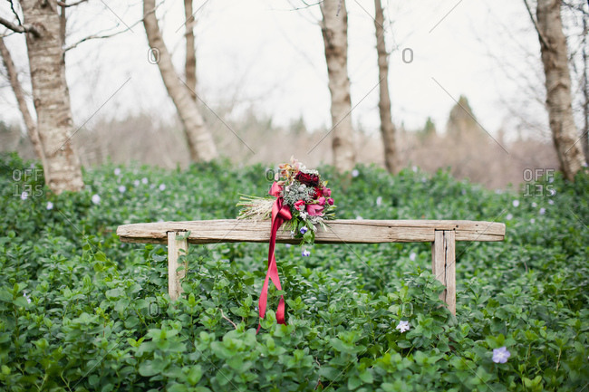Burgundy wedding bouquet resting on rustic wooden bench in forest
