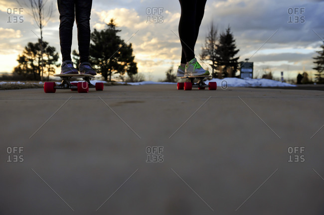Two kids riding skateboards on a later winter afternoon