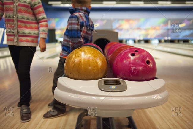 Children standing next to a bowling ball return at a bowling alley