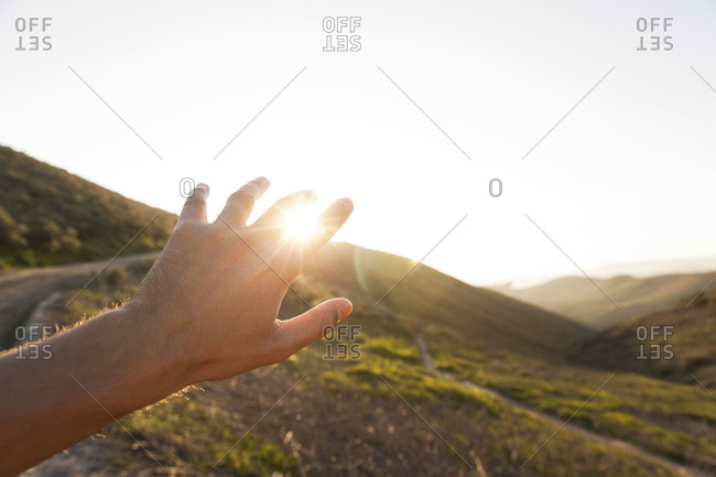 Hand reaching towards the sun at sunset
