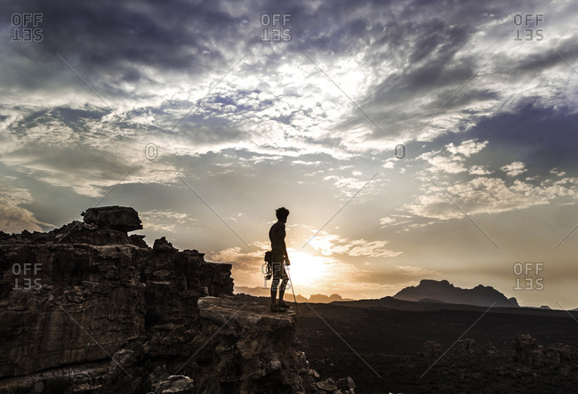 Rock climber silhouetted on top of cliff at dawn