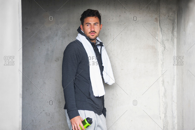 Exhausted young male runner leaning against wall with water bottle