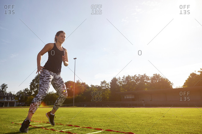 Young woman training on agility ladder on grass