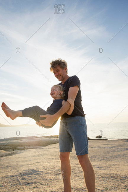 Mature man swinging his toddler daughter on beach, Calvi, Corsica, France