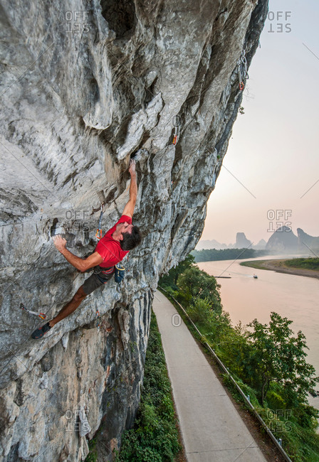 Male climber climbing Riverside crag in Yangshuo, Guangxi Zhuang, China