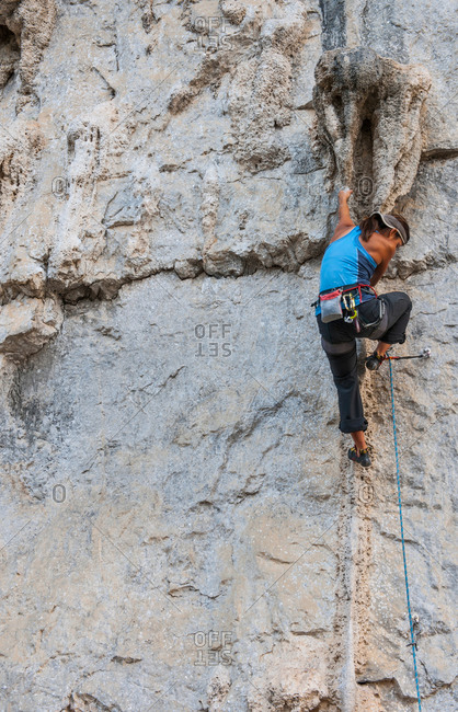 Female climber climbing on Riverside crag - a limestone cliff in Yangshuo, Guangxi Zhuang, China