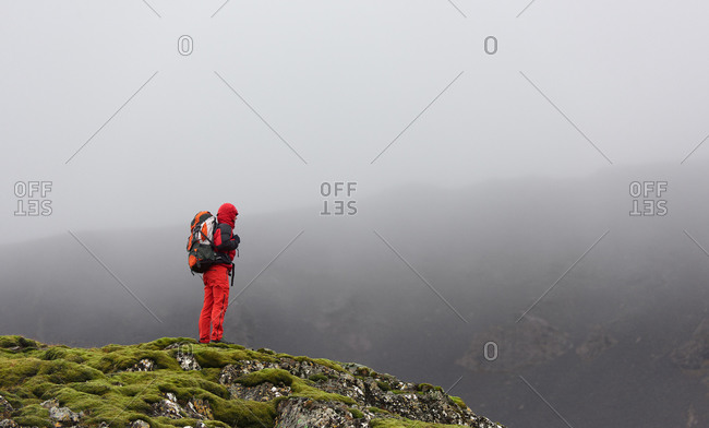 Hiker looking out into a valley on a mossy plateau with dark grey misty clouds in the background