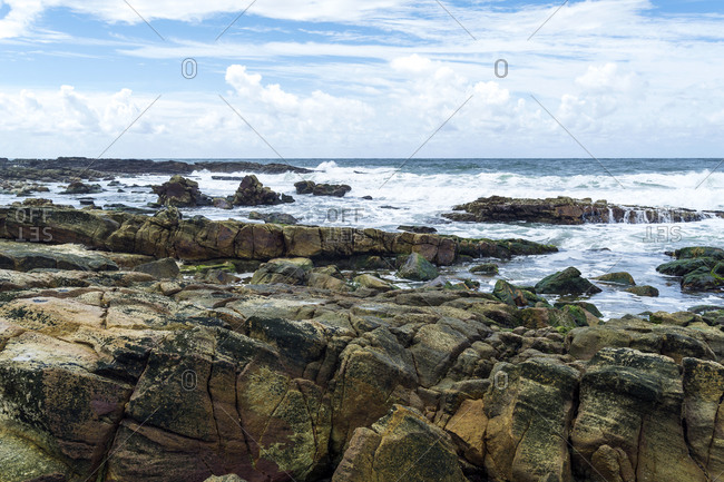 Waves wash over tidal pools and rock slabs on a rugged coastline