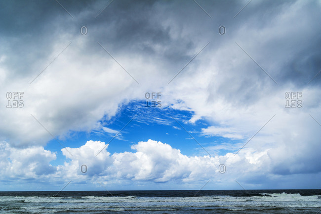 A patch of blue sky appears over an ocean during a storm