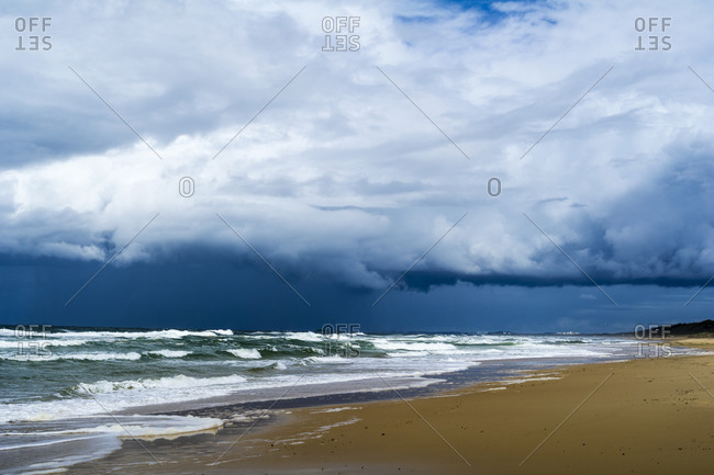 Ominous black storm clouds roll in over waves rolling onto an empty beach