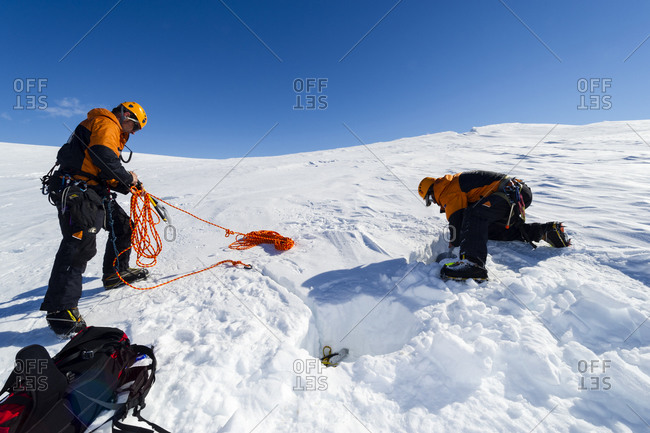 Ice guides digging snow anchors to hold ropes to enter a crevasse on the slopes of Mount Erebus in Antarctica
