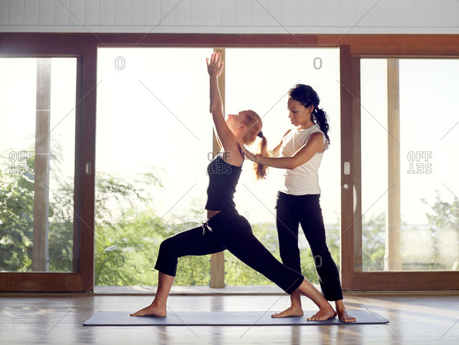 Yoga instructor helping a student with warrior pose during a yoga class