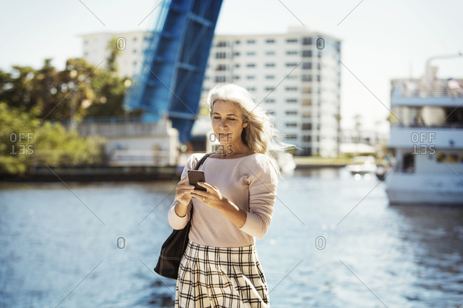 Woman using her smartphone outside near a scenic waterfront